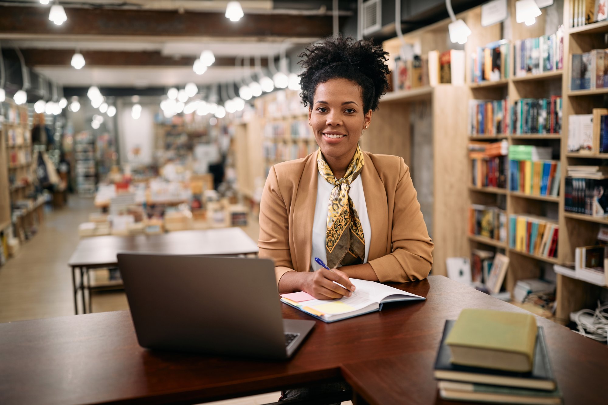 happy-black-university-teacher-sitting-in-a-librar-2023-11-27-05-21-45-utc